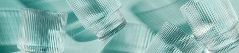 Ribbed crystal glasses casting long shadows on a pale teal surface