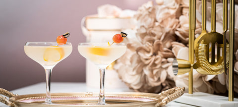 Two crystal coupes with a pale cocktail and a cherry on a gold tray, a matching pair for two