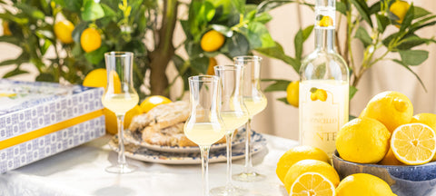 Bicchieri da limoncello in cristallo con limoni freschi e una bottiglia di limoncello sfocata