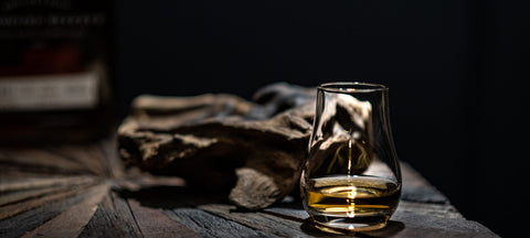 A tulip-shaped whiskey glass with amber spirit on dark driftwood