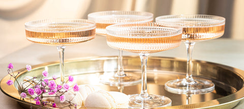 Ribbed pink crystal coupe glasses on a gold tray with macarons and dried flowers