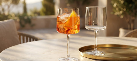 Calice da spritz in cristallo con ghiaccio e fetta d'arancia su un tavolo di marmo chiaro