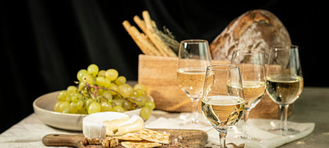 An autumn table with bread, grapes, cheese and stemmed wine glasses of red and white wine