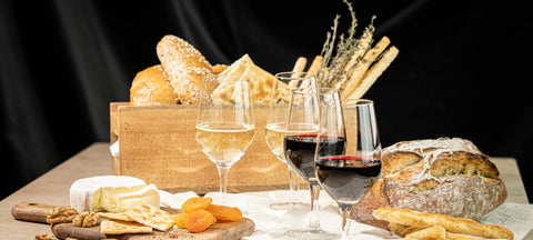A harvest table with bread, cheese, dried apricots and glasses of white and red wine in stemmed tasting glasses