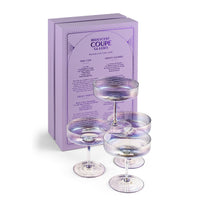 Four iridescent coupe glasses with a purple tint, displayed in front of their lavender packaging box on a white background.