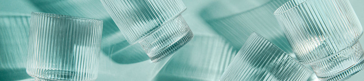 Ribbed crystal glasses casting long shadows on a pale teal surface