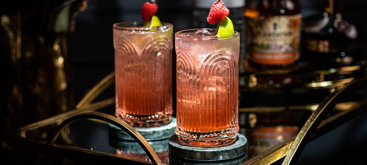 Two garnished cocktails in ribbed Art Deco glasses on a gold bar cart