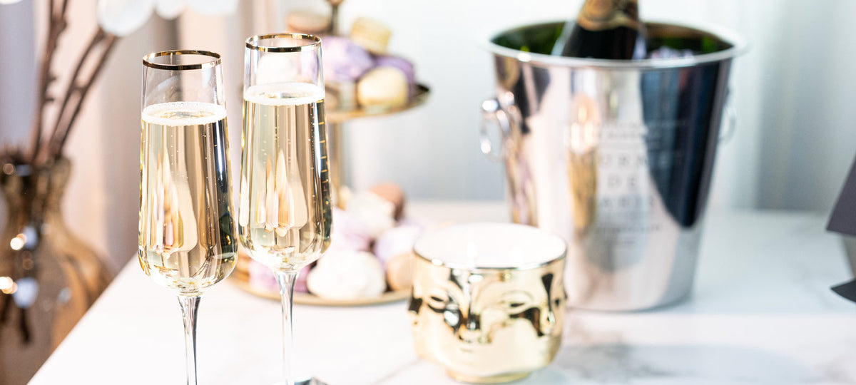 Two gold-rimmed champagne flutes beside an ice bucket on a white table, a toast for newlyweds