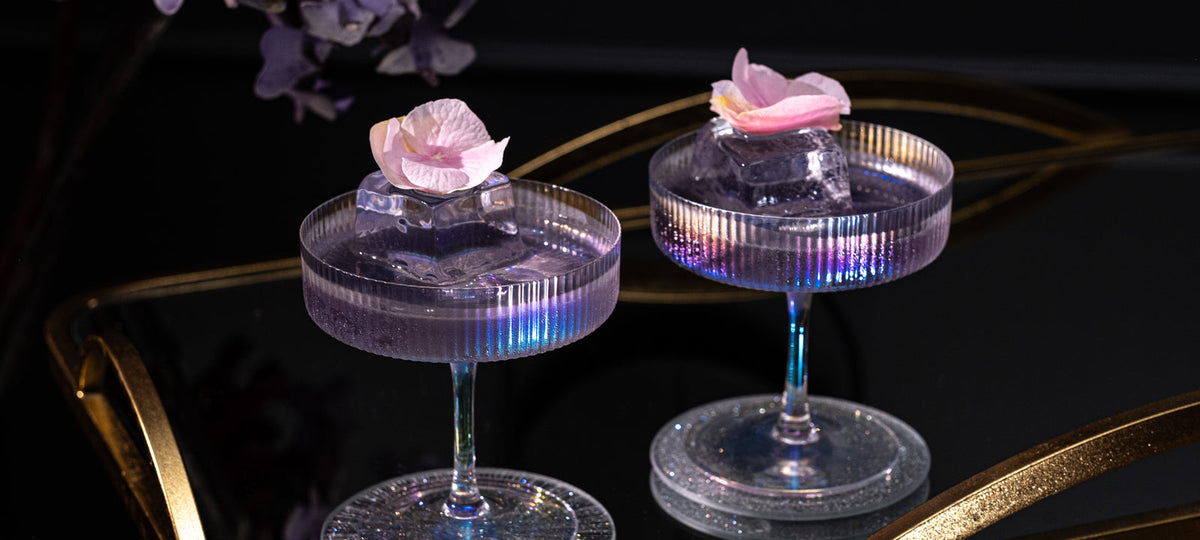 Two iridescent ribbed Art Deco coupes with rose petals on a gold bar cart