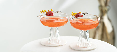 Two strawberry cocktails in ribbed Paris coupes on a white marble table