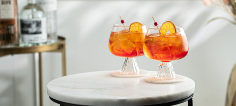 Zwei orange Spritz-Drinks mit Orangenscheibe und Eis in gerippten Stielgläsern auf einem Marmortisch