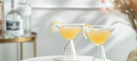 Two sugar-rimmed sidecars with lemon twist in fluted coupe glasses on a white marble table