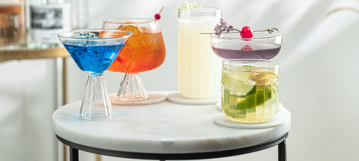 Five cocktail glass shapes side by side, each holding a different drink, on a marble table