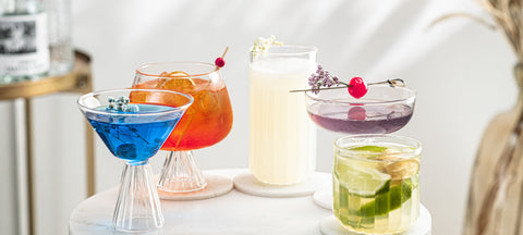 Vier Cocktailglasformen nebeneinander: Martiniglas, Longdrinkglas, Coupe und Lowball, jeweils gefüllt