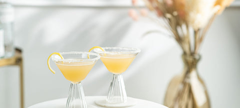 Two sugar-rimmed cocktails with lemon twists in ribbed stemmed glasses on a white table