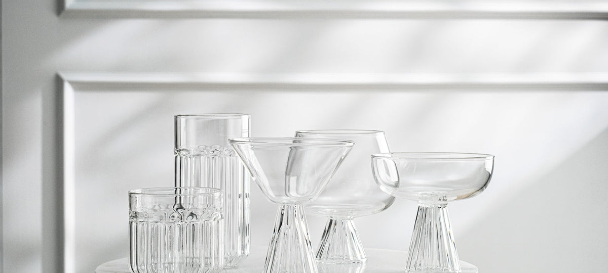 A lineup of clear crystal glasses in several shapes, highball, lowball, coupe and goblet, on a white shelf