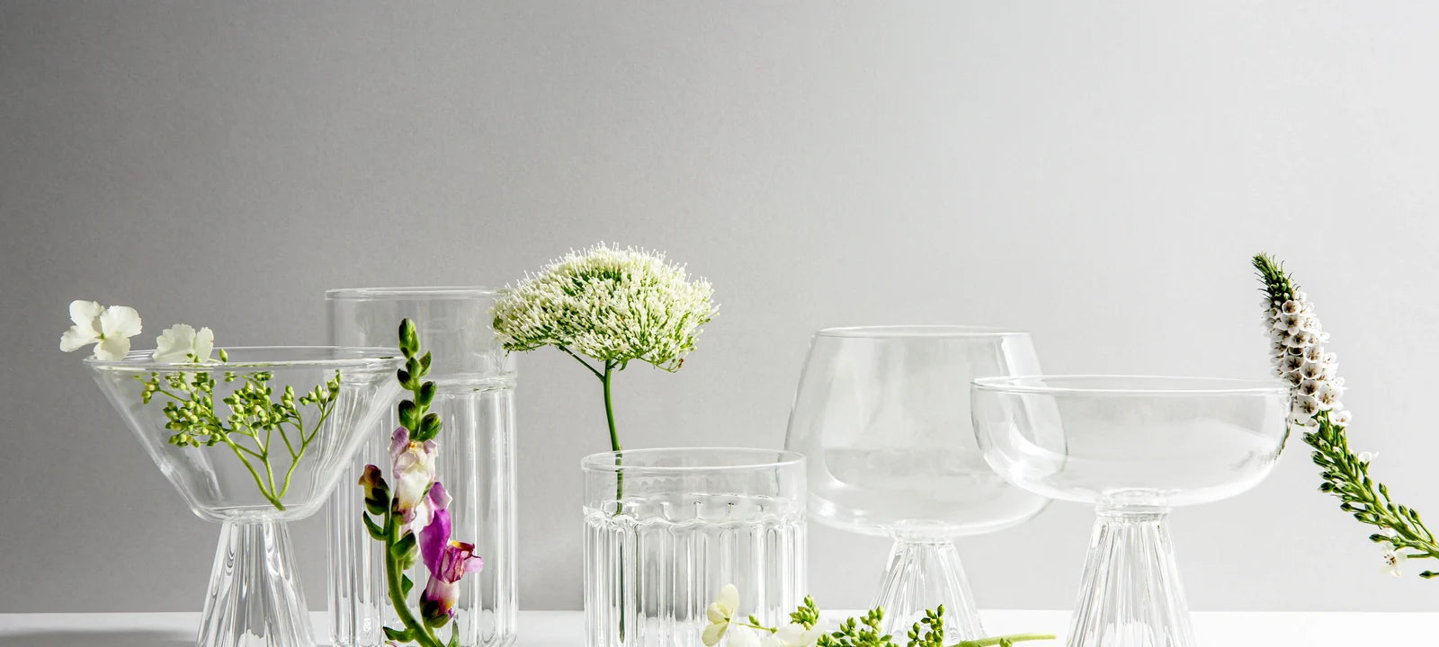 Coupe, martini and Nick and Nora glasses displayed side by side with flowers
