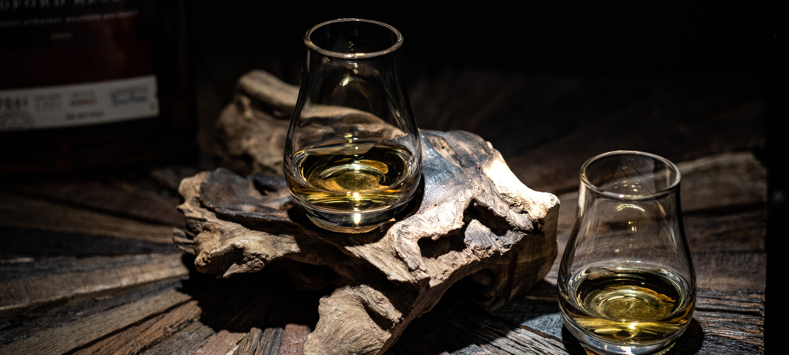 Two whiskey tasting glasses with amber spirit on dark wood in low warm light