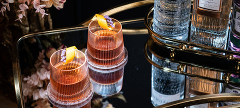 Two Sazeracs with lemon twist in amber ribbed Art Deco lowball glasses on a gold bar cart