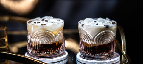 Two Art Deco ribbed lowball glasses with dark cocktails over crushed ice on a gold bar cart