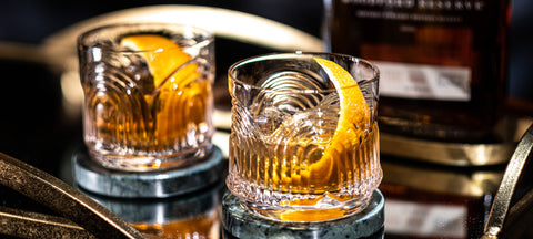 Two Art Deco rocks glasses with an Old Fashioned and a wide orange peel over ice on a gold bar cart
