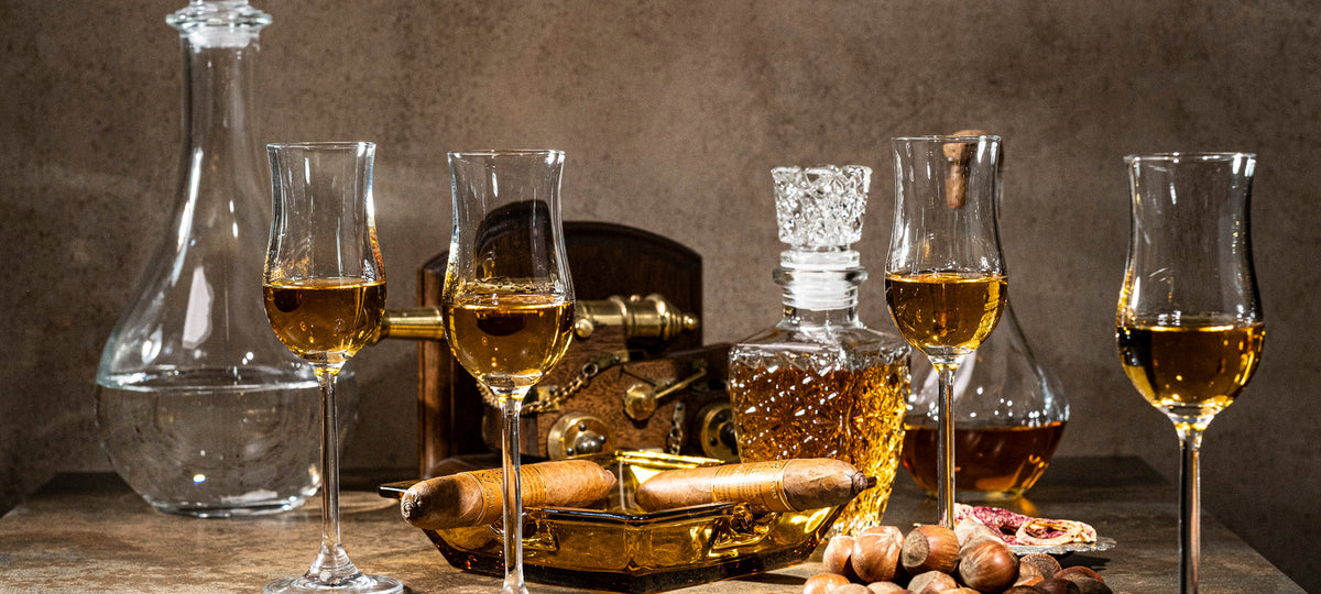 Verres de dégustation tulipe remplis de spiritueux ambré avec une carafe et un cigare sur une table en pierre