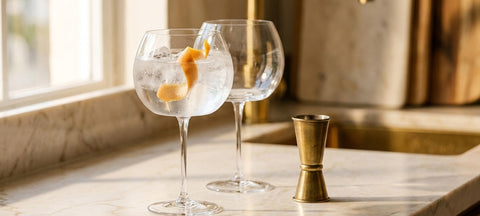Copa de balón in cristallo con gin tonic e ghiaccio su un piano di marmo chiaro