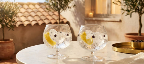 Dos copas de balon estriadas con gin tonic, piel de limon y bayas de enebro sobre una mesa de marmol en una terraza espanola