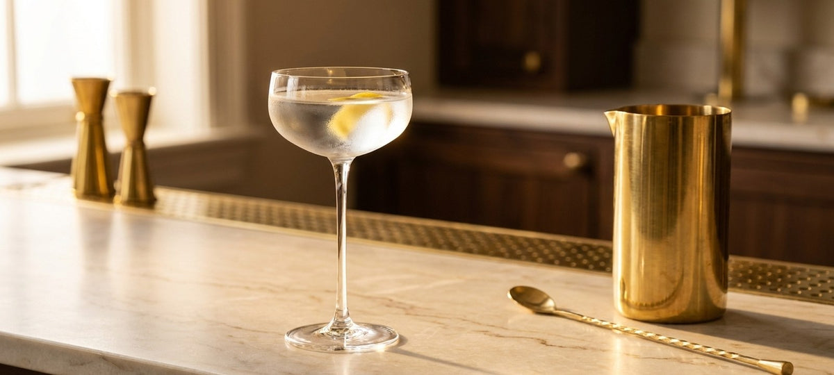 Nick-&-Nora-Glas mit klarem, eiskaltem Martini und Zitronenzeste auf hellem Marmor neben einem Messing-Rührglas