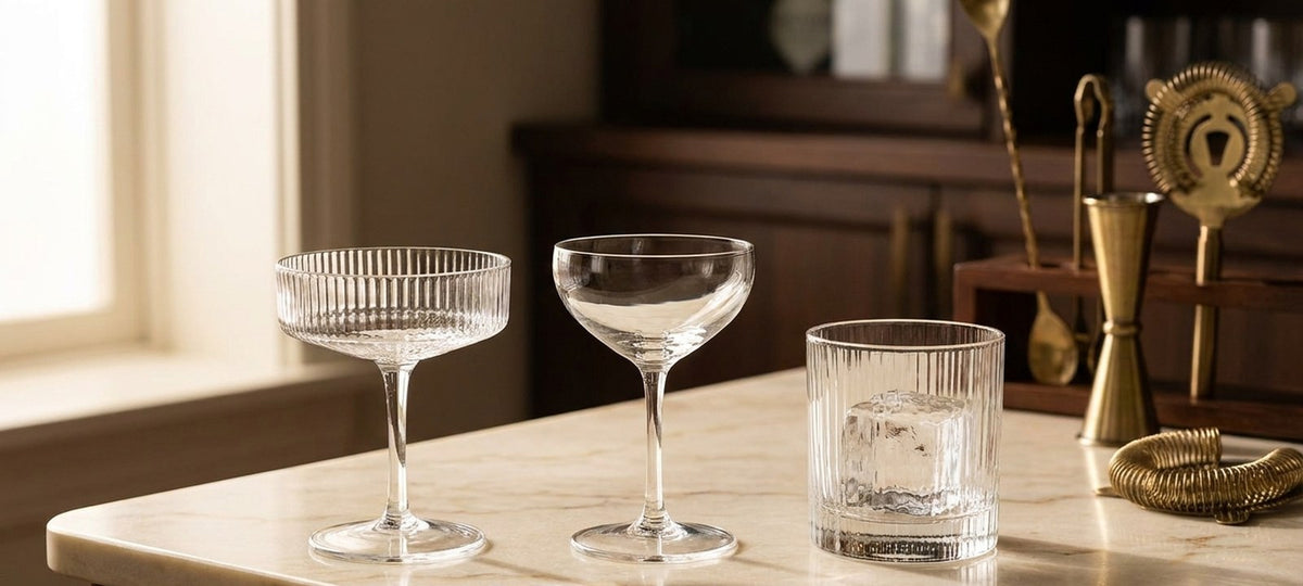 Trois types de verres à cocktail en cristal, coupe Art déco, Nick & Nora et lowball, sur un plan de marbre crème