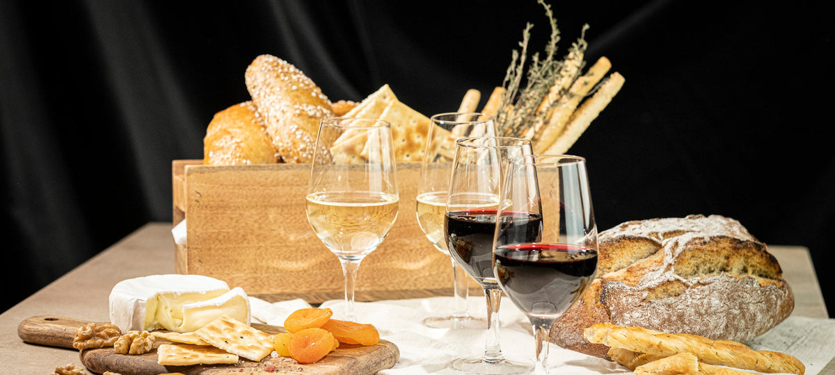 A harvest table with bread, cheese, dried apricots and glasses of white and red wine in stemmed tasting glasses