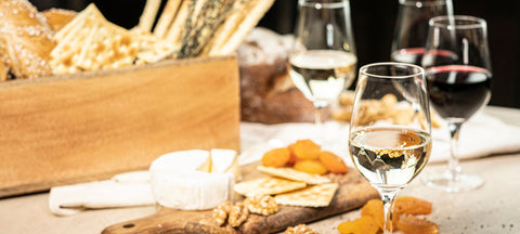 Stemmed glasses of white and red wine on a linen table with bread, cheese and dried apricots