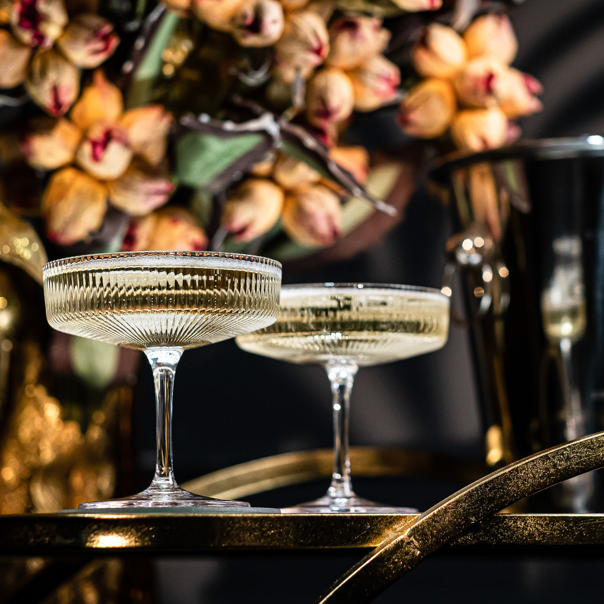 Champagne coupes with gold rims on a gold bar cart in candlelight